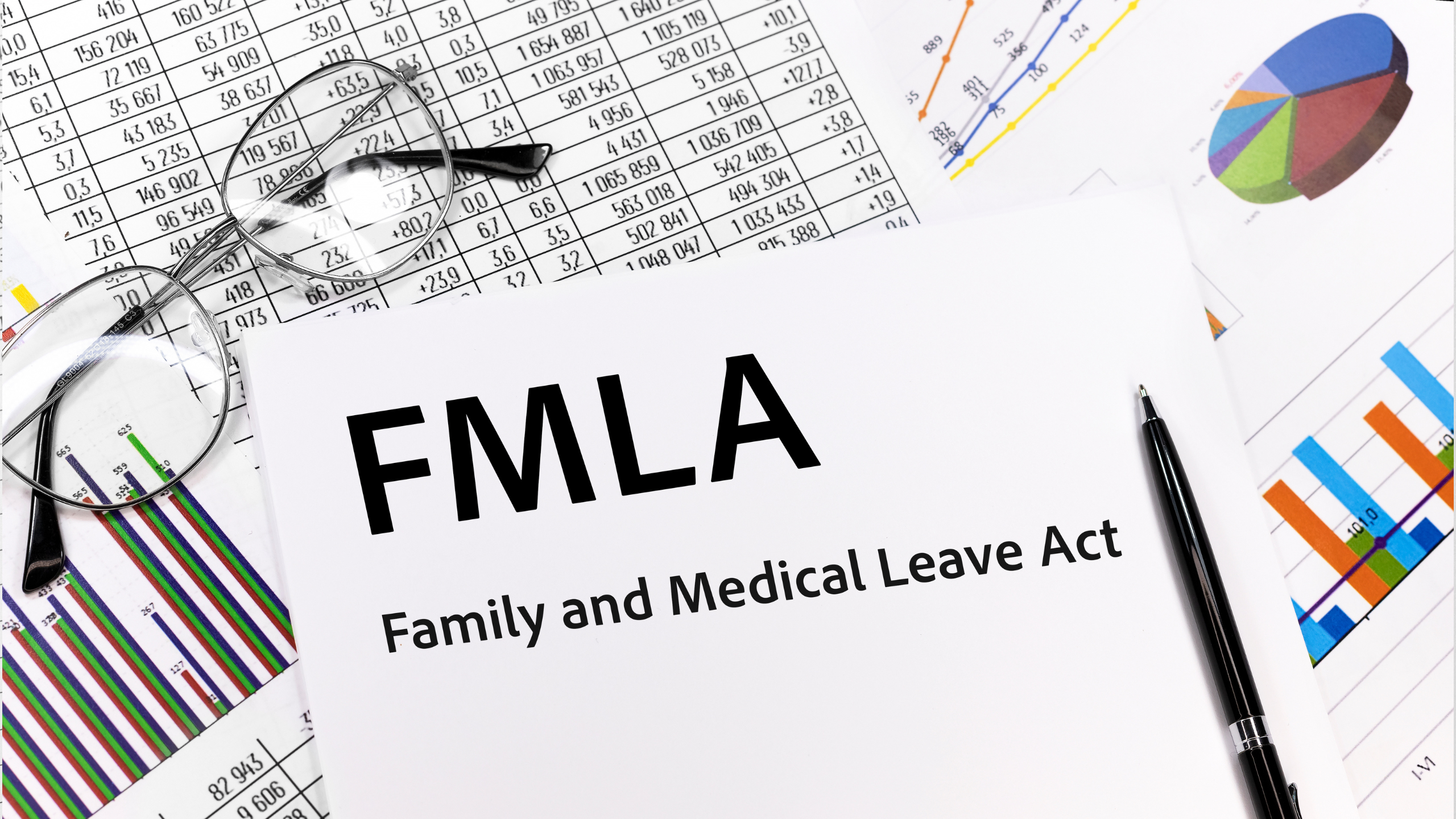 FMLA paperwork with eyeglasses, pen, and data charts on a desk