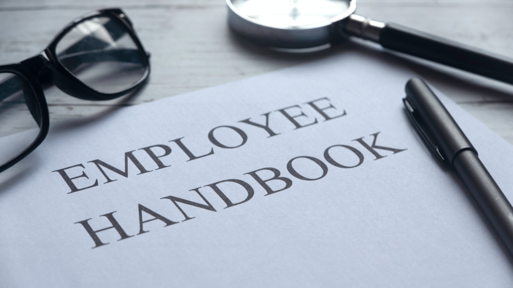 Employee handbook on a desk with a pen and reading glasses