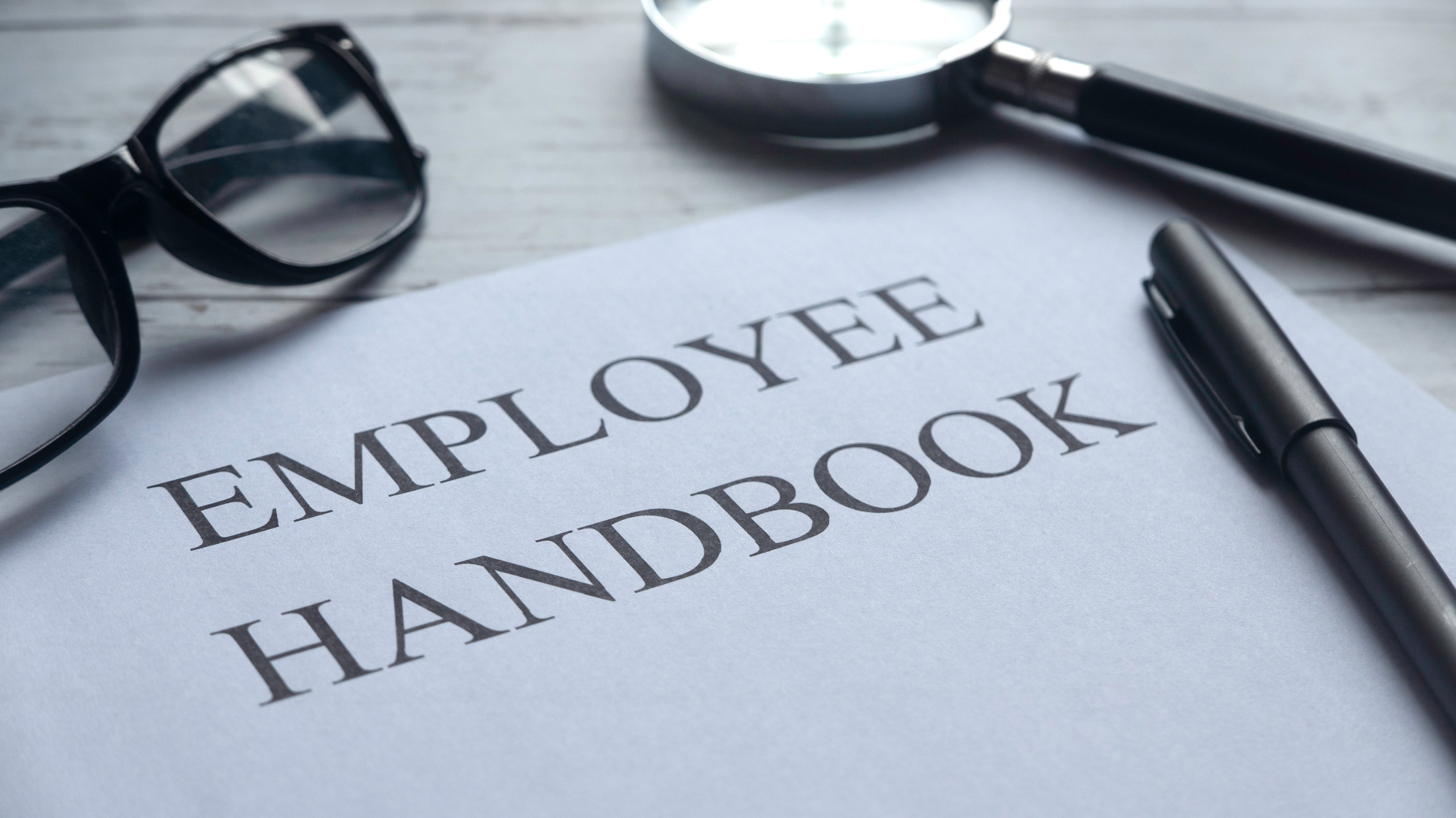 Employee handbook on a desk with a pen and reading glasses