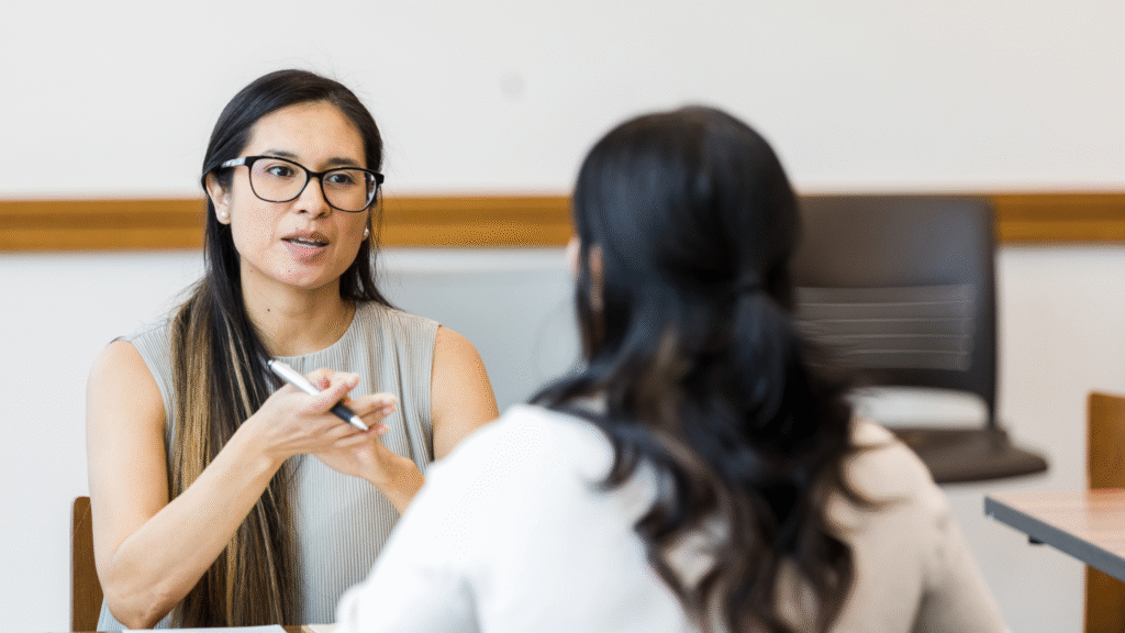 Employee and manager sitting at a desk during a 30-60-90 day review meeting in an office setting.
