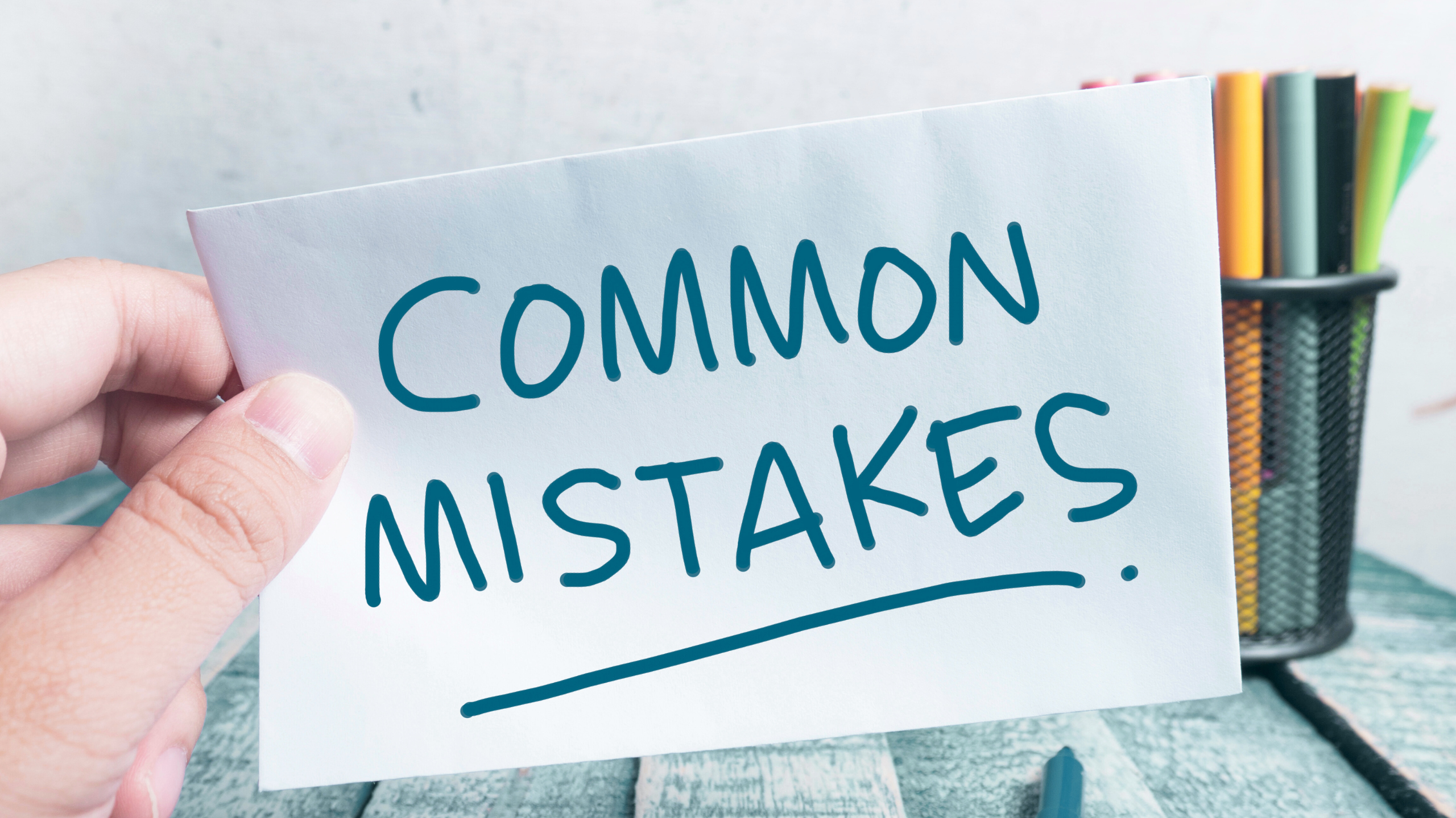 Hand holding a paper with the words "Common Mistakes" written in bold blue marker.