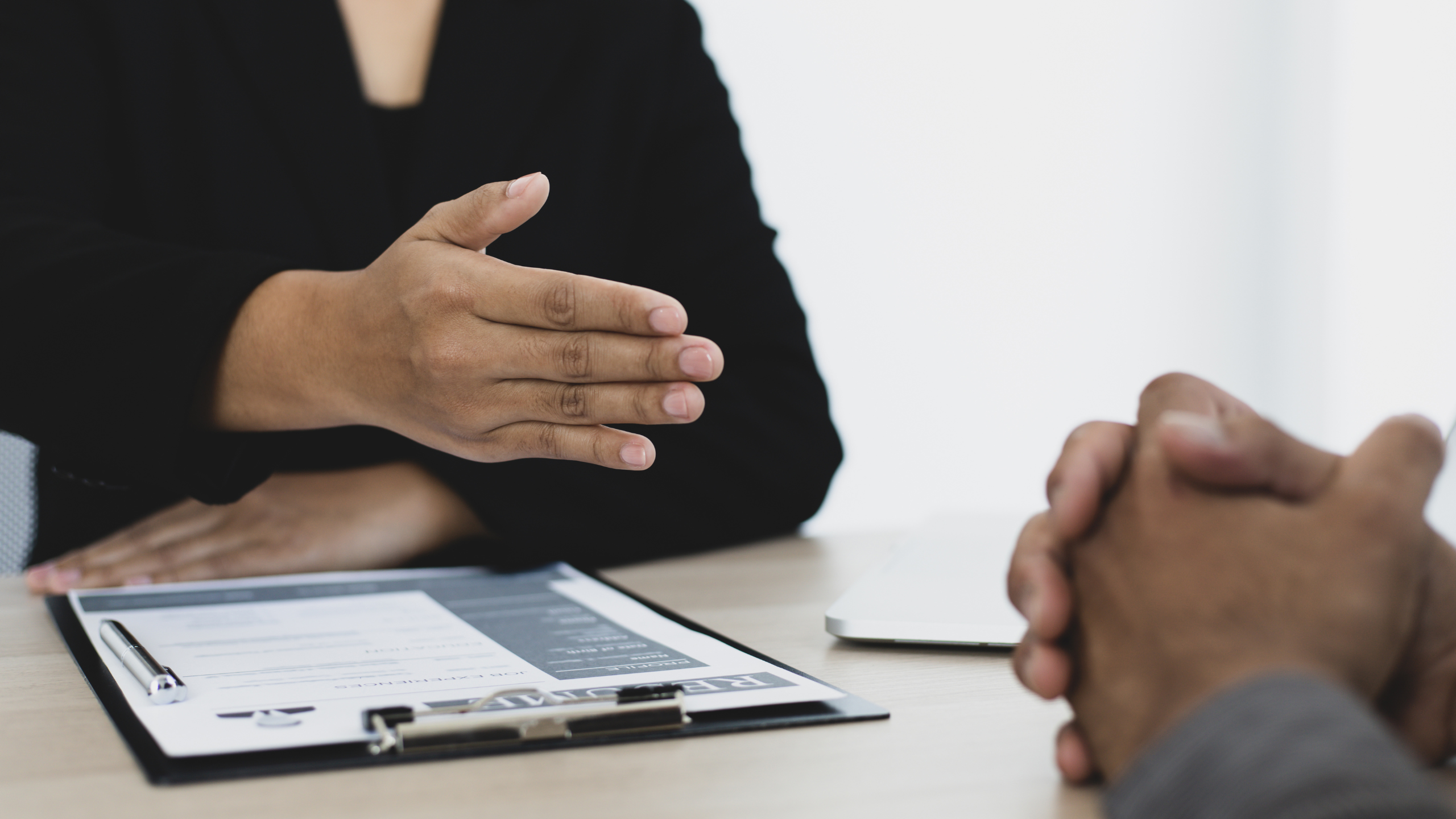 Close-up of a job interview with a hiring manager extending a hand for a handshake across a desk with a resume